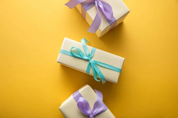 Vista dall'alto di scatole regalo con nastri viola e blu su sfondo giallo — Foto stock