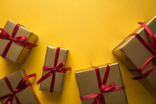 Top view of golden gift boxes with red ribbons on yellow background with copy space — Stock Photo