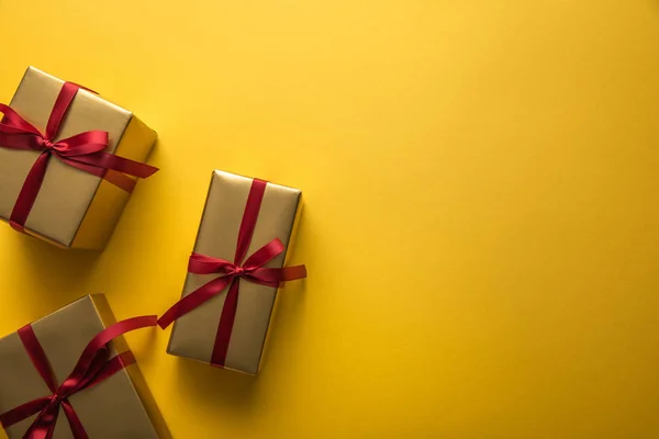 Vista superior de cajas de regalo doradas con cintas rojas sobre fondo amarillo con espacio para copiar — Stock Photo