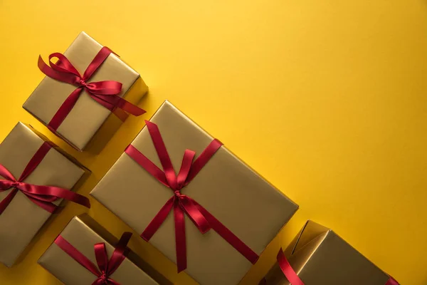 Top view of golden gift boxes with red ribbons on yellow background with copy space — Stock Photo