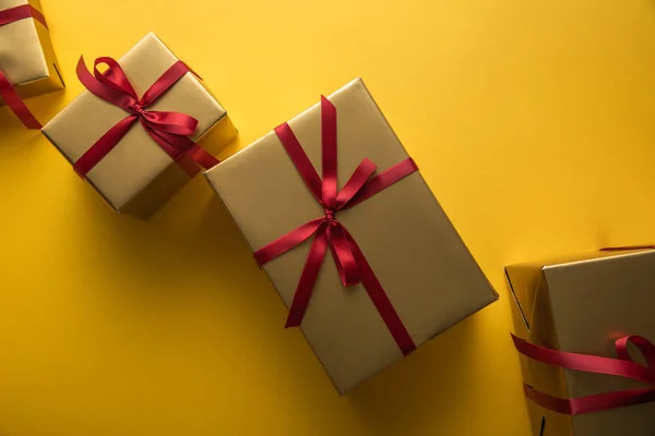 Top view of golden gift boxes with red ribbons on yellow background — Stock Photo