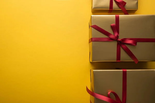 Top view of golden gift boxes with red ribbons on yellow background with copy space — Stock Photo