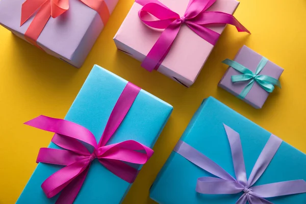 Top view of multicolored gift boxes with ribbons on yellow background — Stock Photo