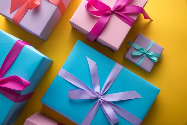 Top view of multicolored gift boxes with ribbons on yellow background — Stock Photo