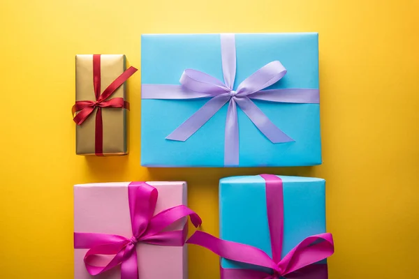 Top view of multicolored gift boxes with ribbons on yellow background — Stock Photo