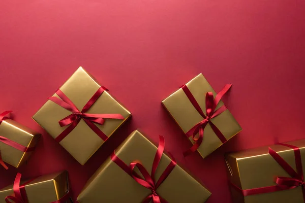 Vue du dessus des boîtes-cadeaux dorées avec des rubans sur fond rouge — Photo de stock