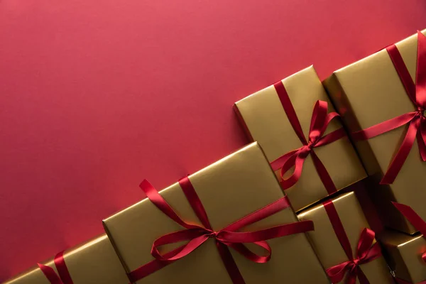 Вид зверху на золоті подарункові коробки зі стрічками на червоному тлі з місцем для тексту — стокове фото