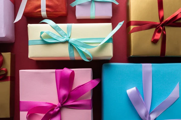 Tendido plano con coloridas cajas de regalo con cintas sobre fondo rojo — Stock Photo