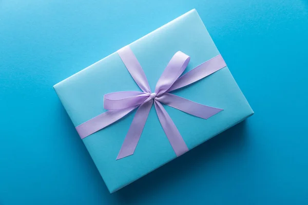 Top view of gift box with violet ribbon on blue background — Stock Photo