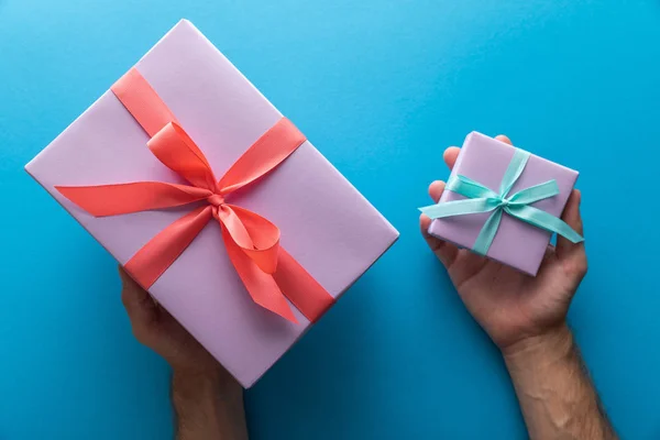 Cropped view of man holding violet gift boxes with ribbons on blue background — Stock Photo