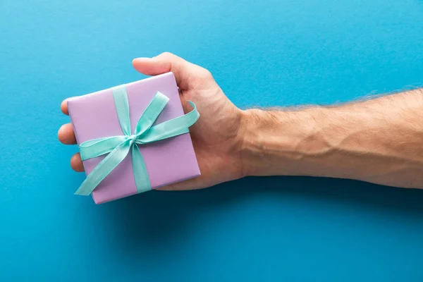 Cropped view of man holding violet gift box on blue background — Stock Photo