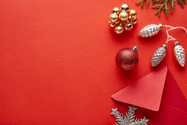 Vista superior da decoração de Natal brilhante, envelope e thuja no fundo vermelho com espaço de cópia — Fotografia de Stock