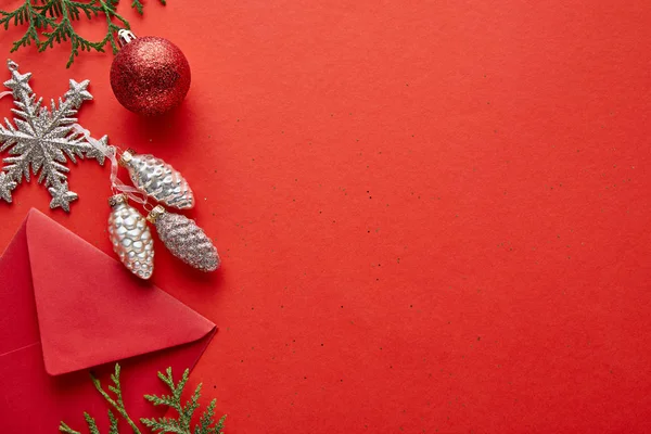 Vue de dessus de la décoration de Noël brillante, enveloppe et thuja sur fond rouge avec espace de copie — Photo de stock