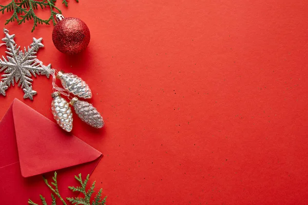 Vista dall'alto della decorazione di Natale lucido, busta e thuja su sfondo rosso con spazio copia — Foto stock