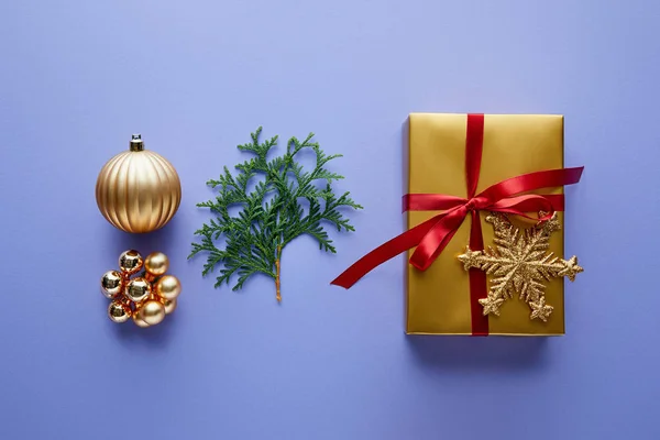 Вид зверху на блискучу золоту різдвяну прикрасу, зелені гілки туї та подарункову коробку на синьому фоні — стокове фото