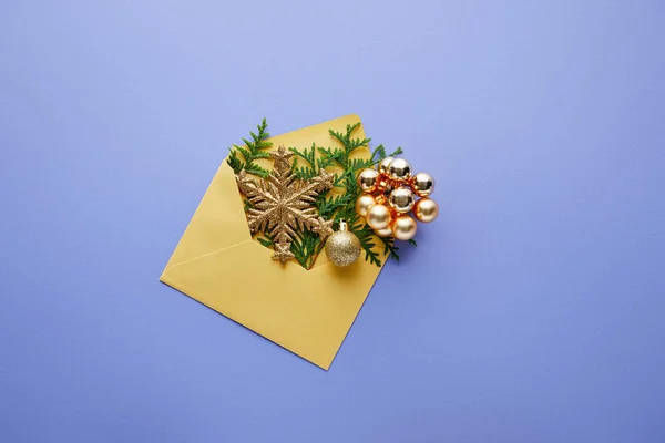 Верхний вид конверта с блестящей золотой рождественской отделкой и зелеными ветвями туи на синем фоне — стоковое фото