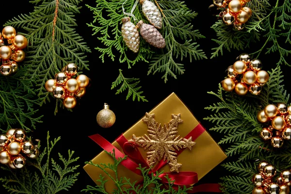 Vue de dessus de la décoration de Noël dorée brillante, branches de thuja vert et boîte cadeau isolé sur noir — Photo de stock