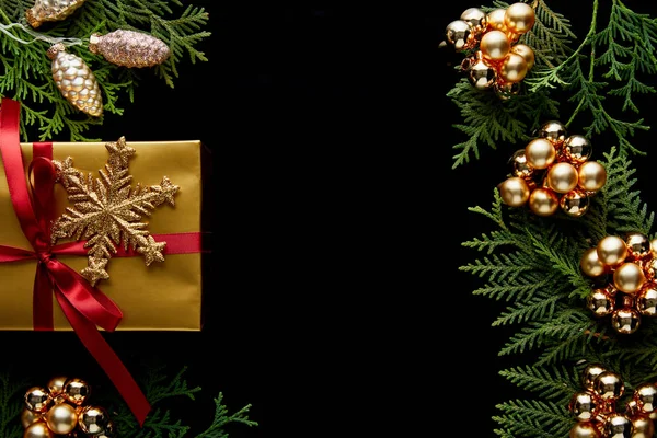 Vista superior de brillante decoración de Navidad dorada, ramas de thuja verde y regalo aislado en negro con espacio de copia - foto de stock