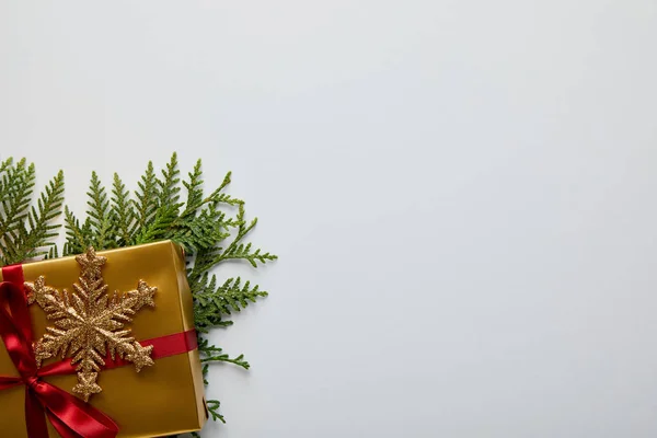 Vista superior de floco de neve dourado brilhante, ramos thuja verde e caixa de presente isolado no branco com espaço de cópia — Fotografia de Stock