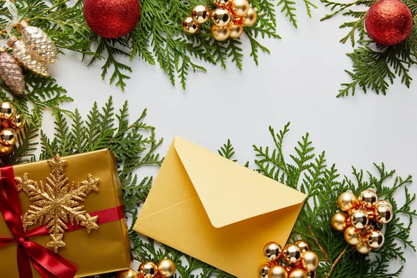 Blick von oben auf goldglänzende Weihnachtsdekoration, Geschenk und Umschlag auf grünen Thuja-Zweigen isoliert auf weiß — Stockfoto