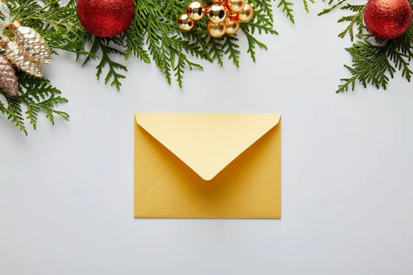 Вид зверху на блискучу золоту різдвяну прикрасу і конверт біля зелених гілок туї ізольовані на білому — стокове фото