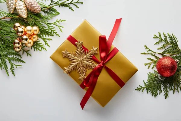 Вид зверху блискуча золота і червона різдвяна прикраса на зелених гілках туї, загорнутий подарунок зі сніжинкою ізольовано на білому — стокове фото