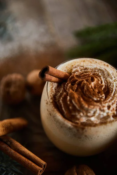 Vue rapprochée de savoureux cocktail au lait de poule avec crème fouettée près des bâtons de cannelle — Photo de stock