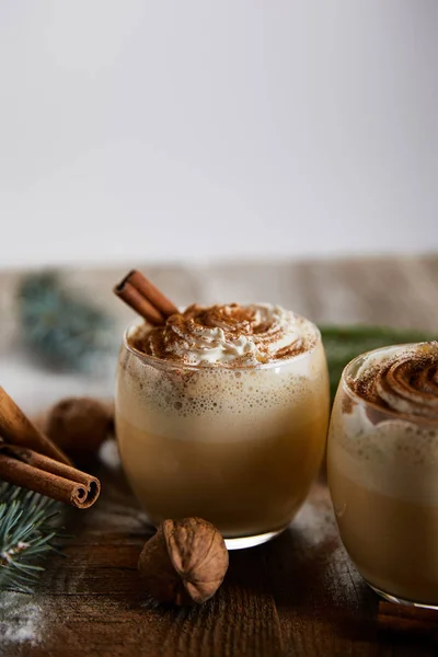 Delicioso cóctel de ponche de huevo con crema batida, palitos de canela y nueces en la mesa de madera aislado en gris - foto de stock