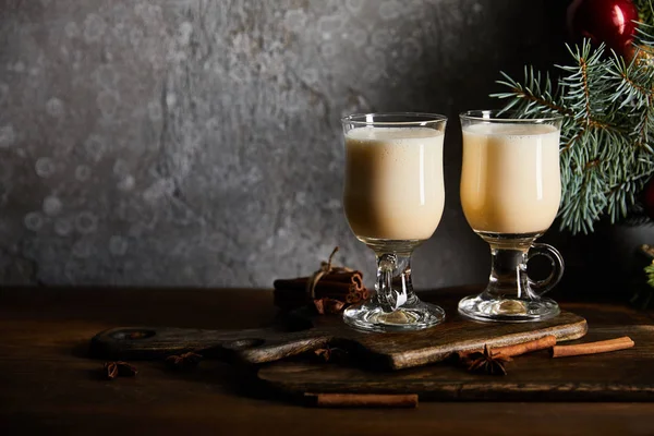 Verres avec boisson au lait de poule délicieuse sur planche à découper près de la branche d'épinette sur fond de pierre grise — Photo de stock