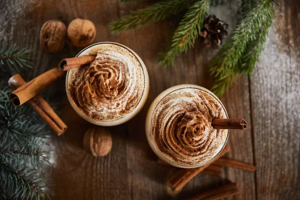 Top view of delicious eggnog drink near spruce branches, wallnuts and cinnamon sticks on wooden table — Stock Photo