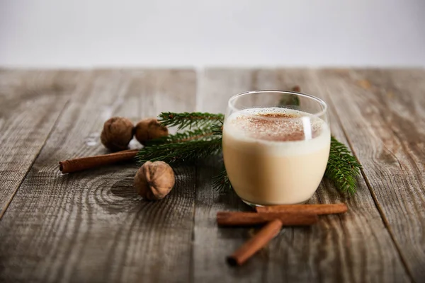 Delicious eggnog cocktail near wallnuts, spruce branch and cinnamon sticks on wooden table isolated on grey — Stock Photo