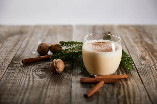 Delizioso cocktail di zabaione vicino a wallnuts, ramo di abete rosso e bastoncini di cannella su tavolo di legno isolato su grigio — Foto stock