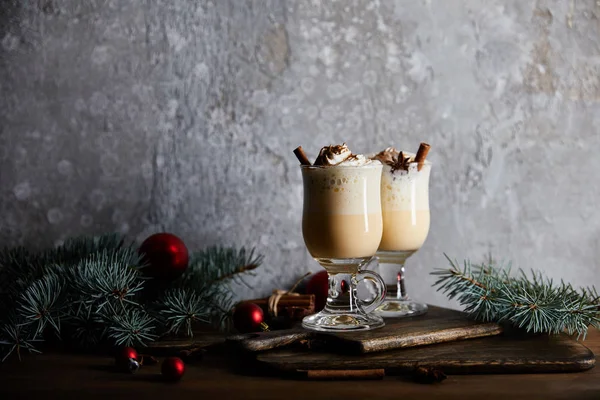 Delicioso coquetel de gemada com chantilly e canela na placa de corte perto de ramos de abeto no fundo de pedra cinza — Fotografia de Stock