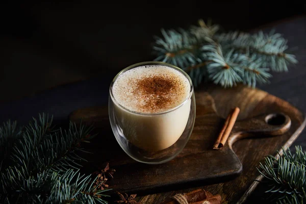 Delicious eggnog cocktail on cutting board near spruce branches and cinnamon sticks isolated on black — Stock Photo