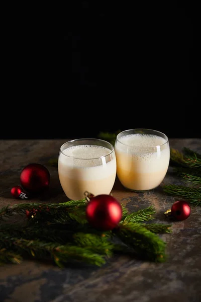 Традиционный коктейль эггног рядом с еловой ветвью и рождественские шарики на мраморной поверхности, изолированной от черного — стоковое фото