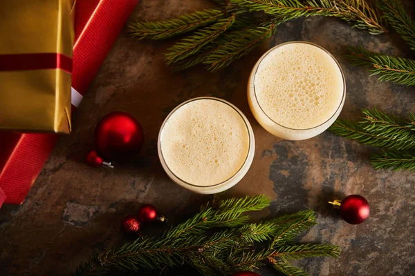 Top view of delicious eggnog cocktail, spruce branches, Christmas balls and gift boxes on dark marble surface — Stock Photo