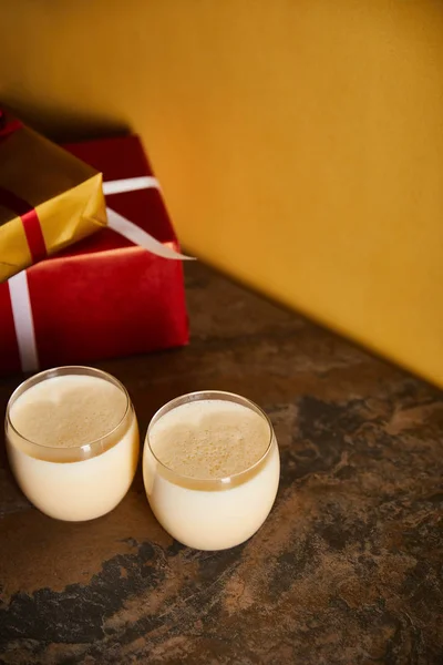 Delicioso cóctel de ponche de huevo y cajas de regalo en mesa de mármol oscuro cerca de la pared naranja - foto de stock