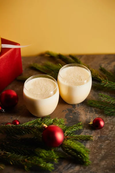 Delicious eggnog cocktail, gift boxes, spruce branches and Christmas balls on dark marble table isolated on orange — Stock Photo
