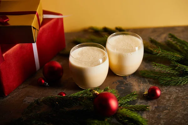 Traditional eggnog cocktail, gift boxes, spruce branches and Christmas balls on dark marble table isolated on orange — Stock Photo