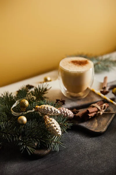 Eggnog cocktail on table covered with sugar powder, spruce branches, cinnamon sticks and Christmas baubles on orange background — Stock Photo