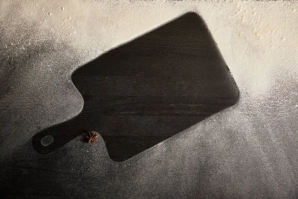 Vue du dessus de la planche à découper noire et de l'anis étoilé sur la table recouverte de sucre en poudre — Photo de stock