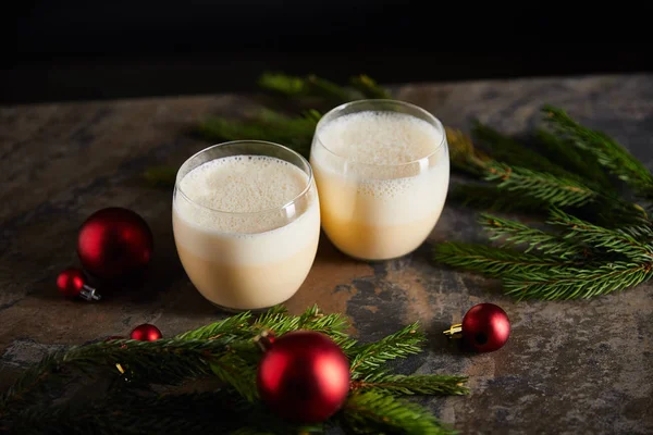 Delicioso cóctel de ponche de huevo, ramas de abeto y bolas de Navidad en mesa de mármol oscuro aislado en negro - foto de stock