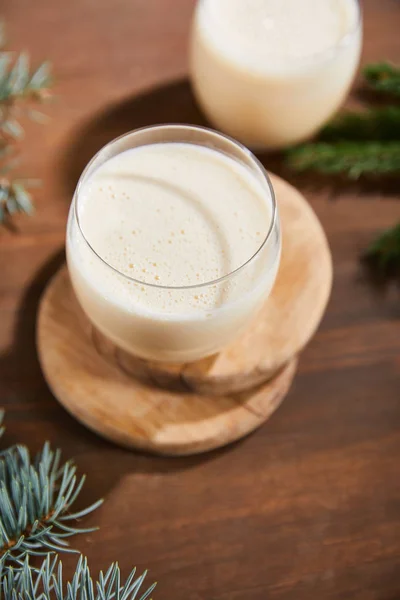 Delizioso cocktail di zabaione su tavole di legno rotonde vicino a rami di abete rosso su tavolo di legno — Foto stock