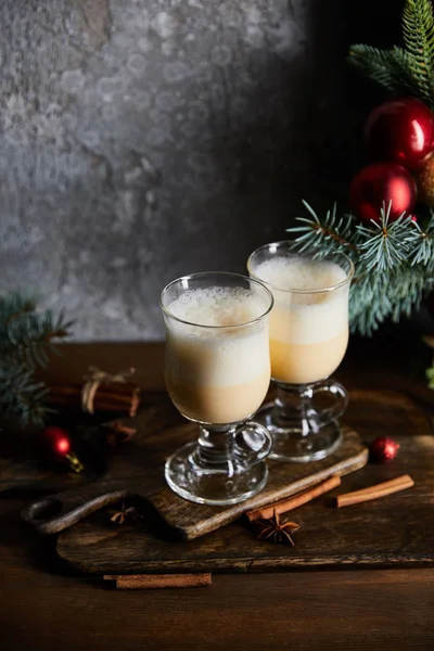 Traditional eggnog cocktail on cutting board near decorated spruce branches on grey stone background — Stock Photo