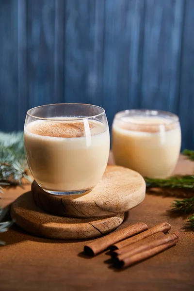 Délicieux cocktail au lait de poule sur des planches rondes en bois près des branches d'épinette et des bâtons de cannelle sur fond texturé bleu — Photo de stock