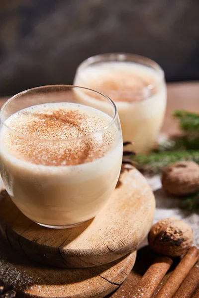 Vista de cerca de delicioso cóctel de ponche de huevo en tablas redondas, palitos de canela y nueces en mesa de madera - foto de stock