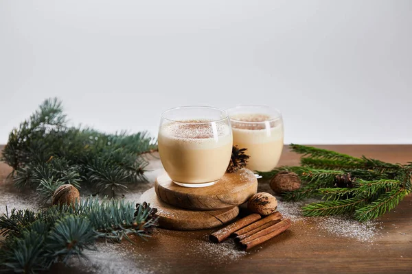 Flavored eggnog cocktail on round boards, spruce branches, cinnamon sticks and walnuts isolated on grey — Stock Photo