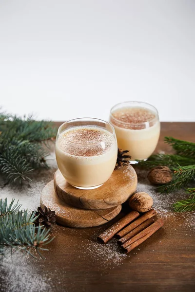 Flavored eggnog cocktail on round boards, spruce branches, cinnamon sticks and walnuts isolated on grey — Stock Photo