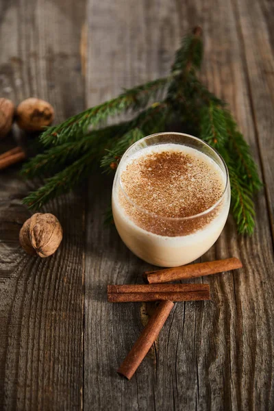 Leckerer Eierlikör-Cocktail neben Fichtenzweig, Zimtstangen und Walnüssen auf Holztisch — Stockfoto