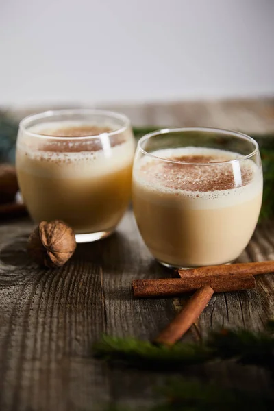 Selective focus of flavored eggnog cocktail near cinnamon sticks and walnuts on wooden table isolated on grey — Stock Photo